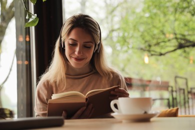Photo of Woman listening to audiobook at table in cafe