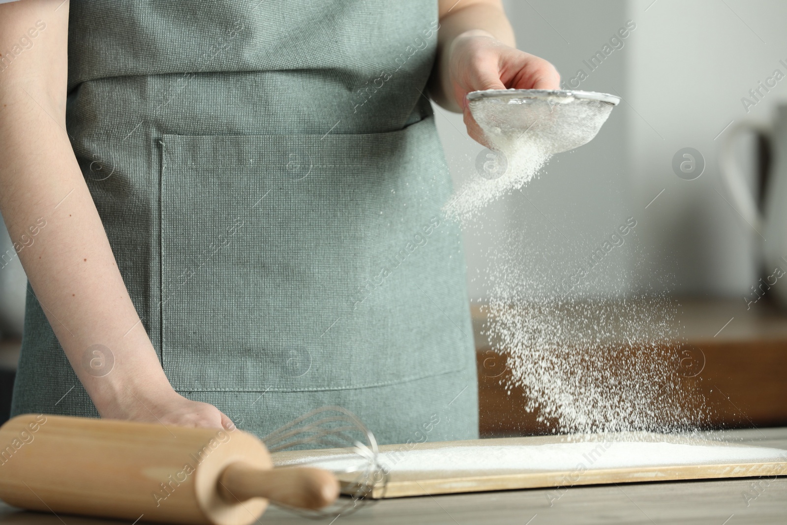 Photo of Woman sieving flour at table in kitchen, closeup