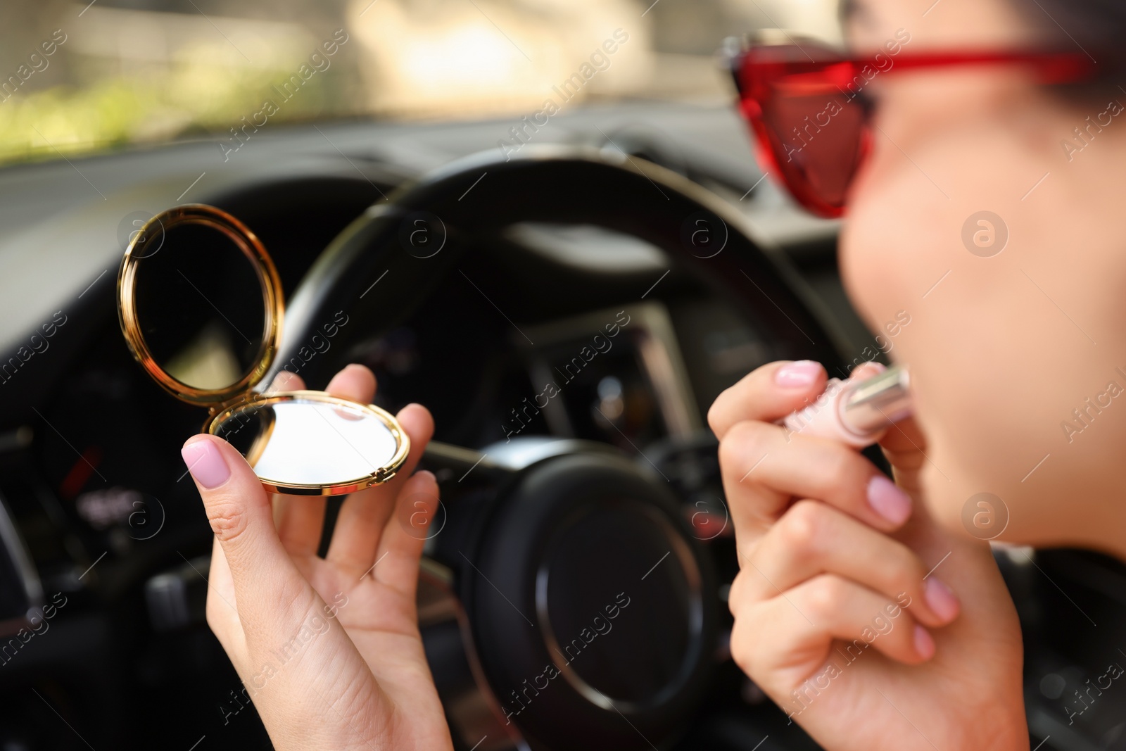 Photo of Beautiful woman with cosmetic pocket mirror applying lipstick in car, closeup