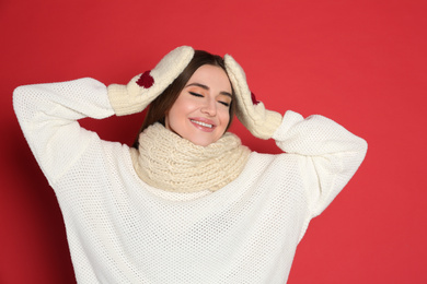 Photo of Young woman wearing warm sweater and mittens on red background. Winter season