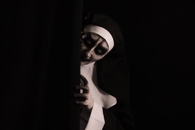 Scary devilish nun hiding on black background, space for text. Halloween party look