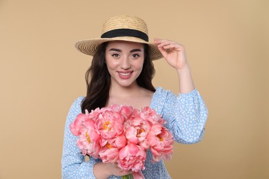 Photo of Beautiful young woman in straw hat with bouquet of pink peonies against beige background