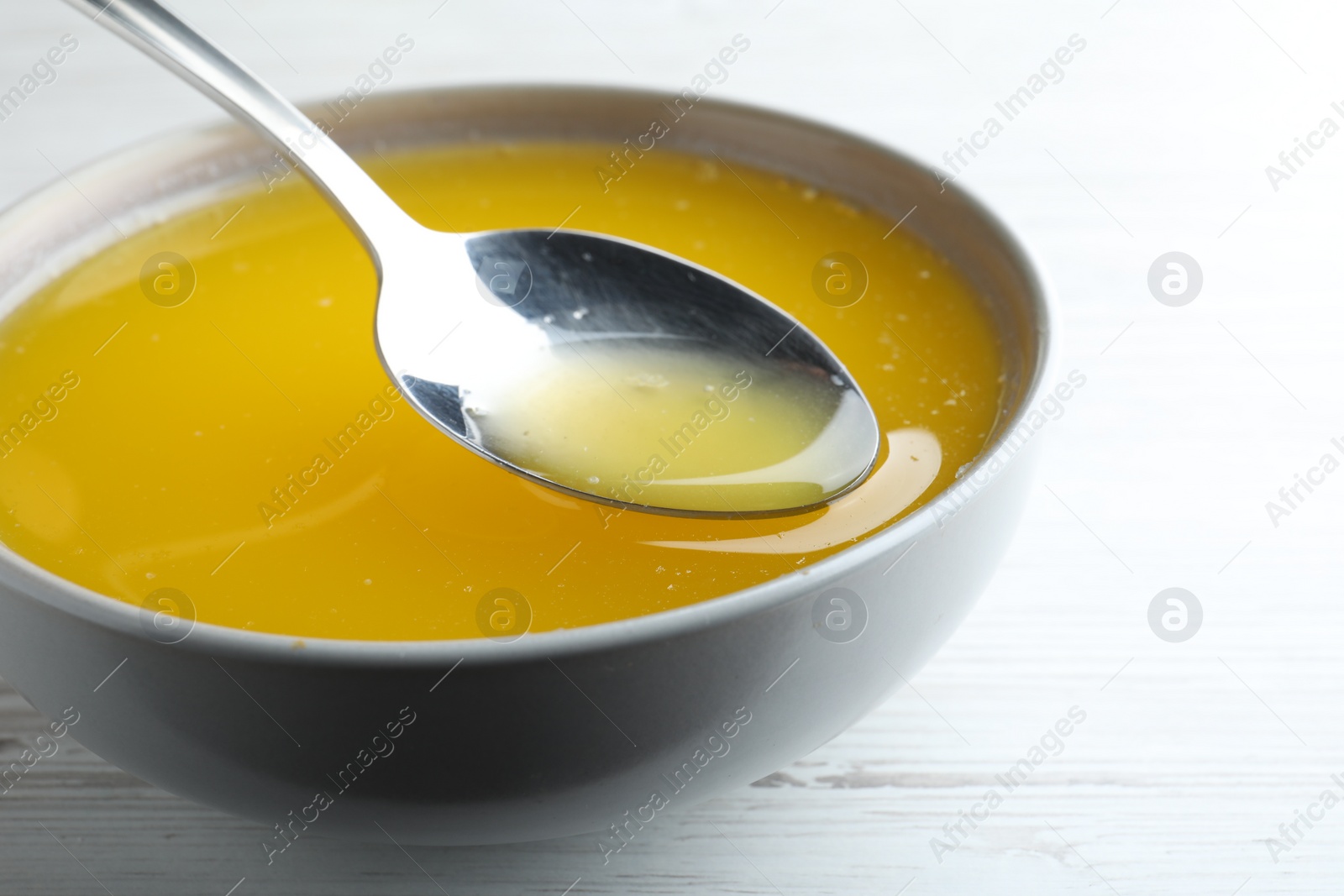 Photo of Spoon of clarified butter over bowl on white wooden table, closeup