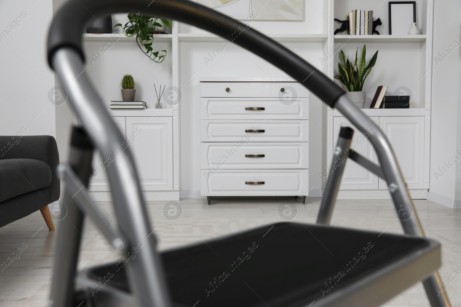 Photo of Chest of drawers near shelving unit, view through metal ladder