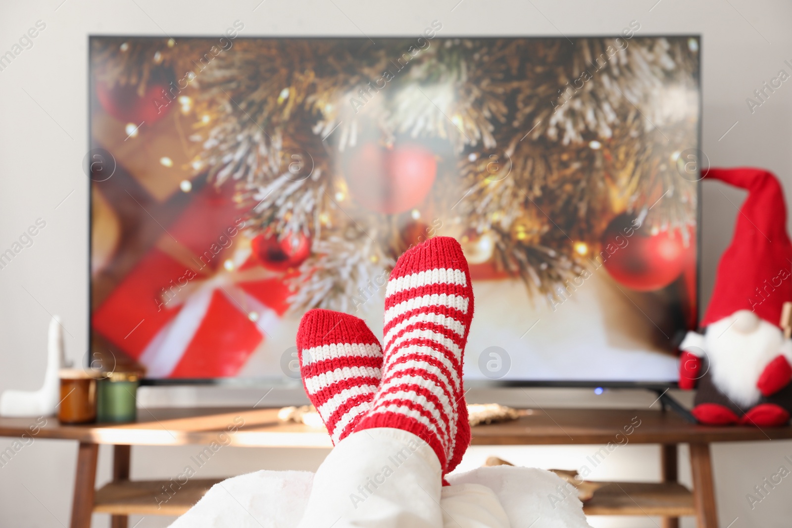 Photo of Woman in cute knitted socks watching TV at home, closeup