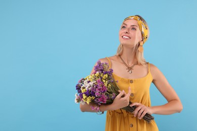Portrait of smiling hippie woman with bouquet of flowers on light blue background. Space for text