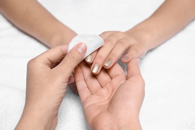 Manicurist removing polish from client's nails on white fabric, closeup
