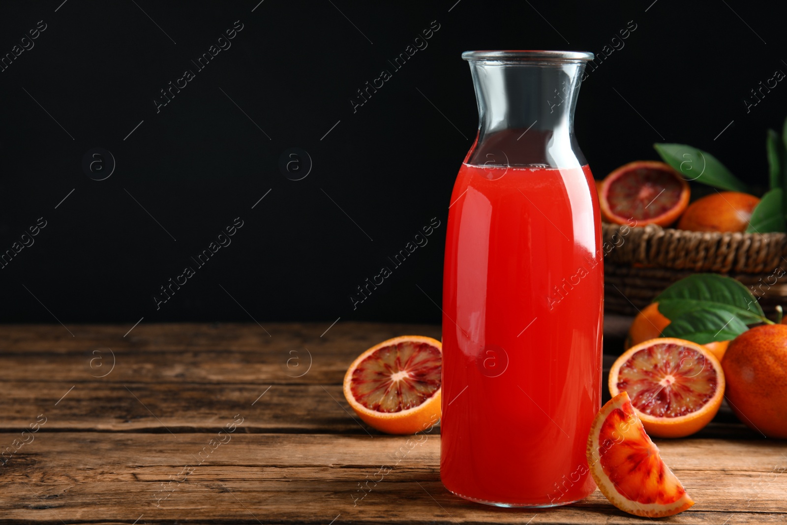 Photo of Tasty sicilian orange juice in glass bottle and fruits on wooden table, space for text