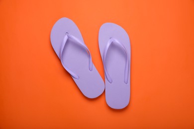Stylish violet flip flops on orange background, top view