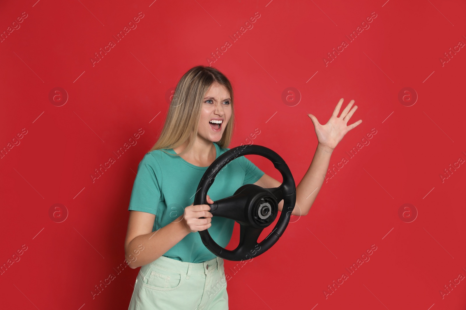 Photo of Emotional young woman with steering wheel on red background