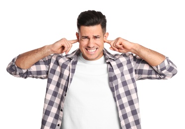 Emotional man covering ears with fingers on white background