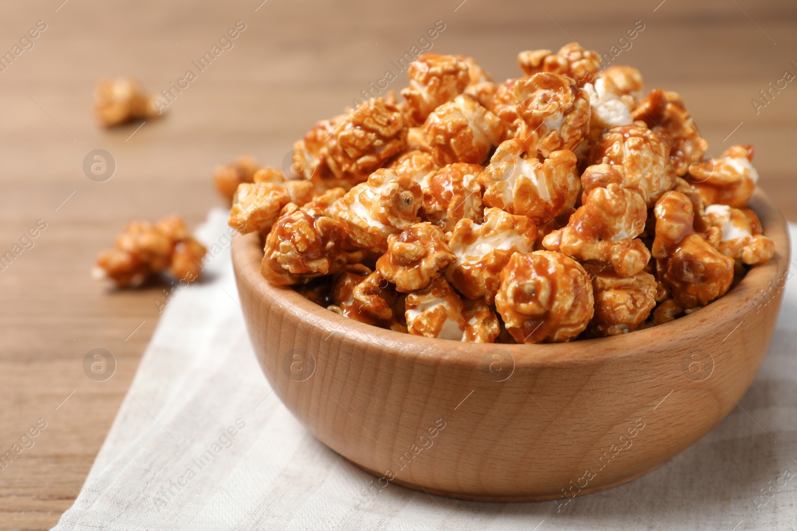 Photo of Wooden bowl with tasty caramel popcorn on table