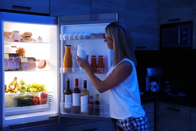 Woman taking bottle with milk out of refrigerator in kitchen at night