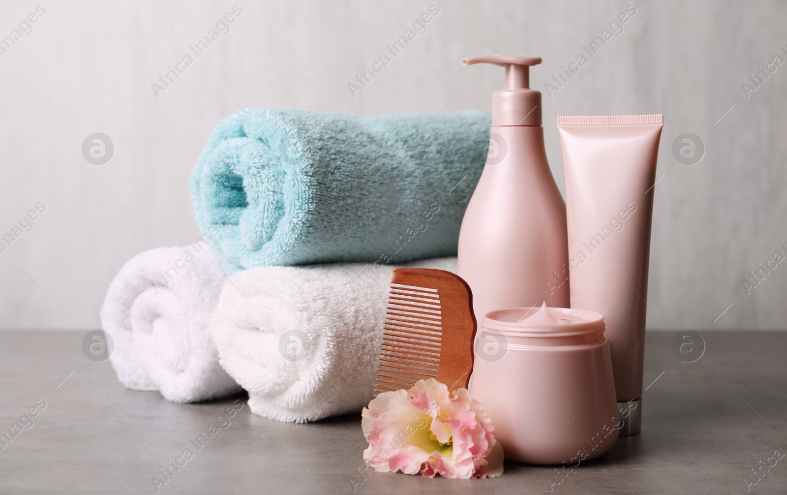 Photo of Different hair products, rolled towels and wooden comb on grey table