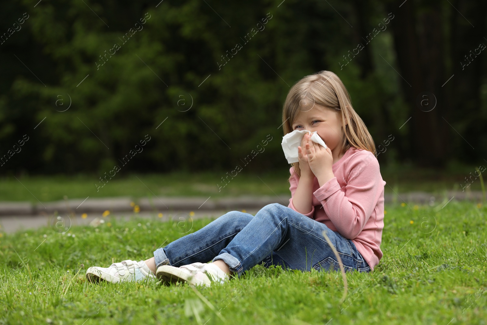 Photo of Little girl suffering from seasonal spring allergy on green grass in park