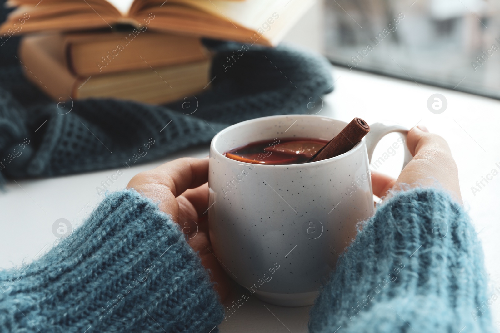 Photo of Woman holding cup of mulled wine near window indoors, closeup. Winter drink