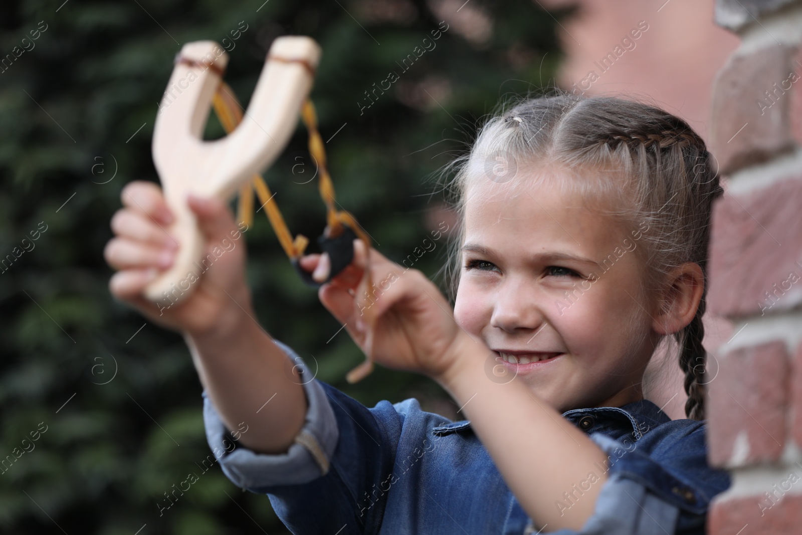 Photo of Little girl playing with slingshot outdoors. Kid's toy