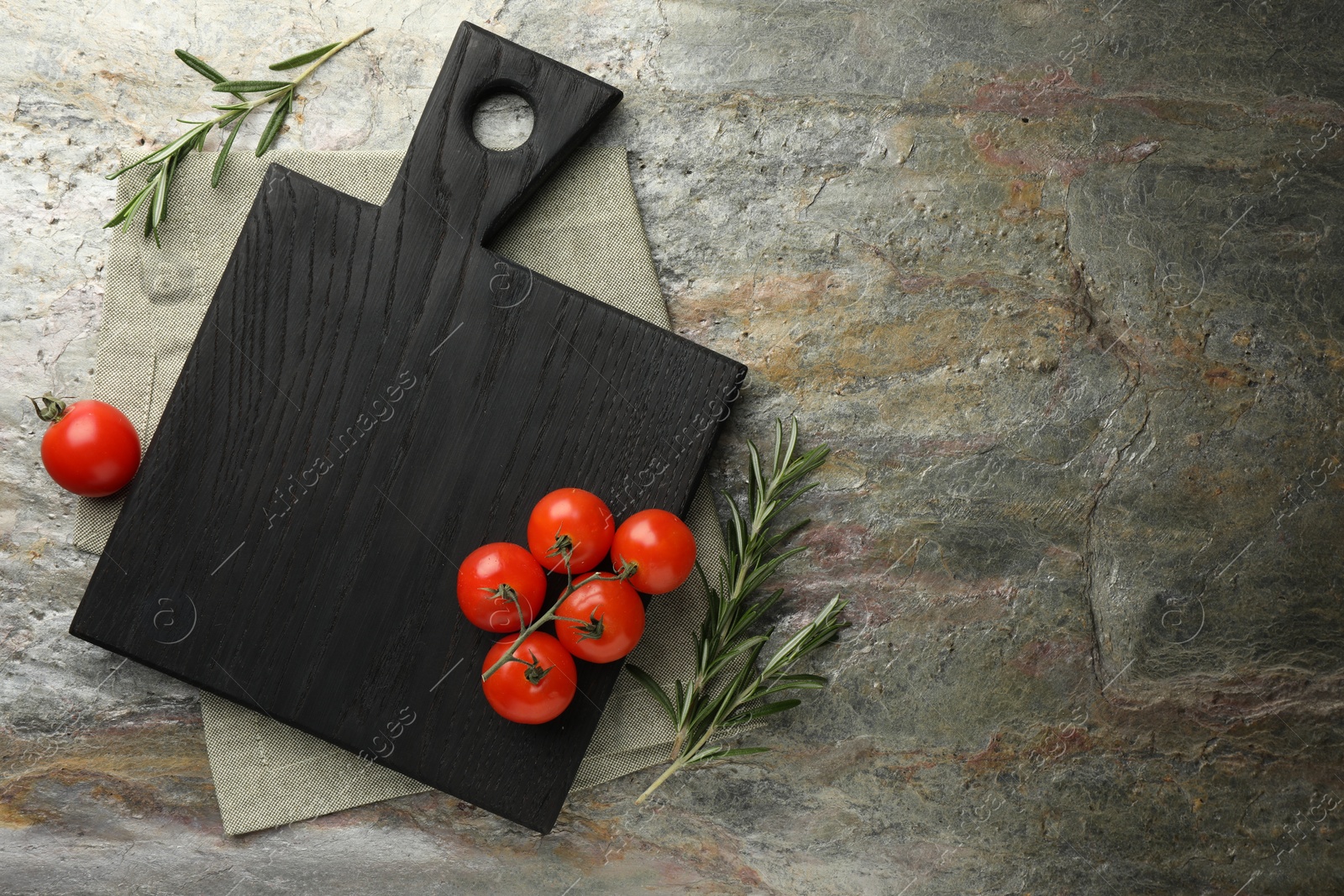 Photo of Black cutting board, tomatoes and rosemary on textured table, flat lay. Space for text