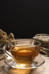 Photo of Freshly brewed tea and dried herbs on wooden table against black background. Space for text