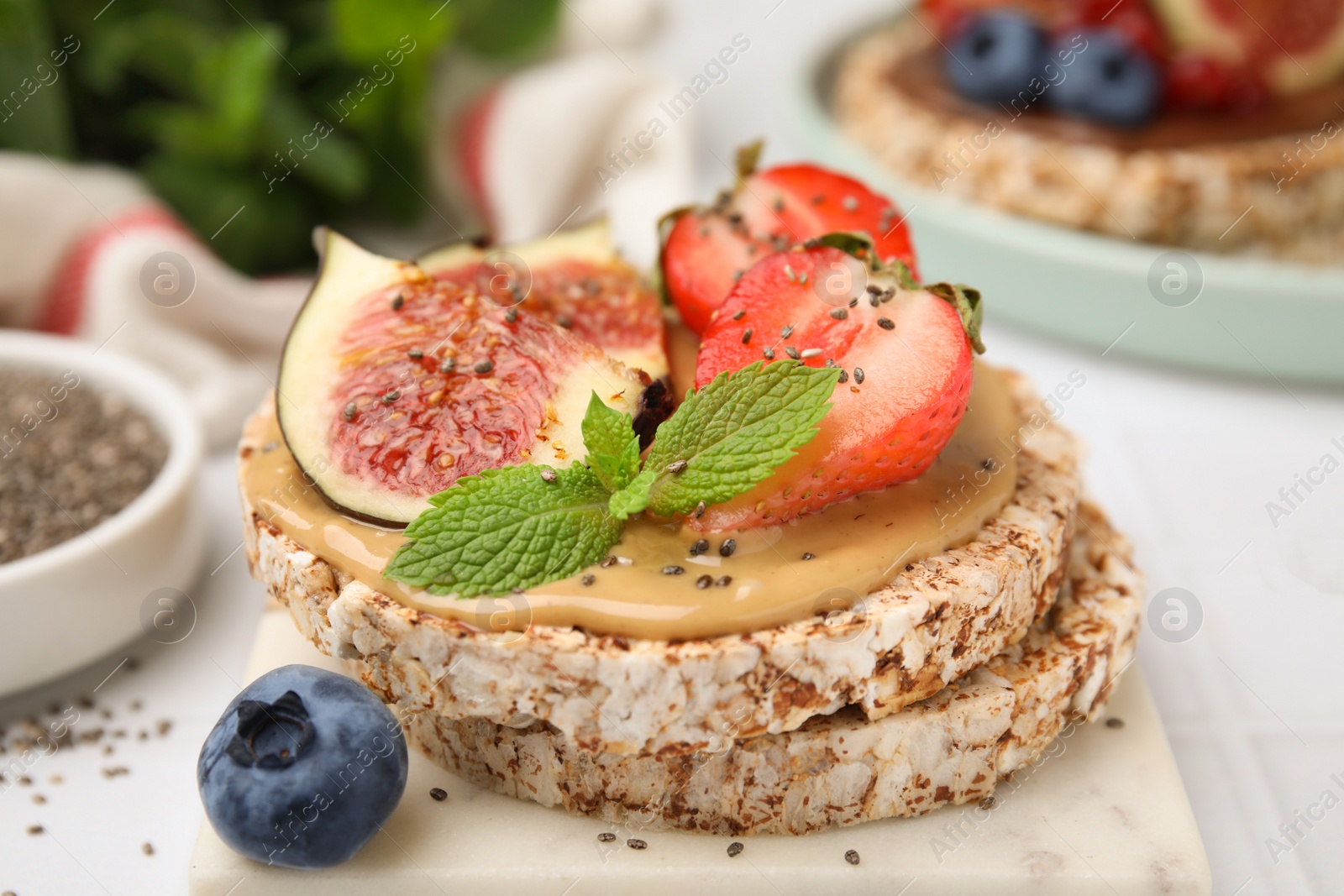 Photo of Tasty crispbreads with peanut butter, figs and berries on light table, closeup