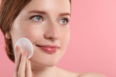 Photo of Beautiful woman with freckles wiping face on pink background, closeup. Space for text