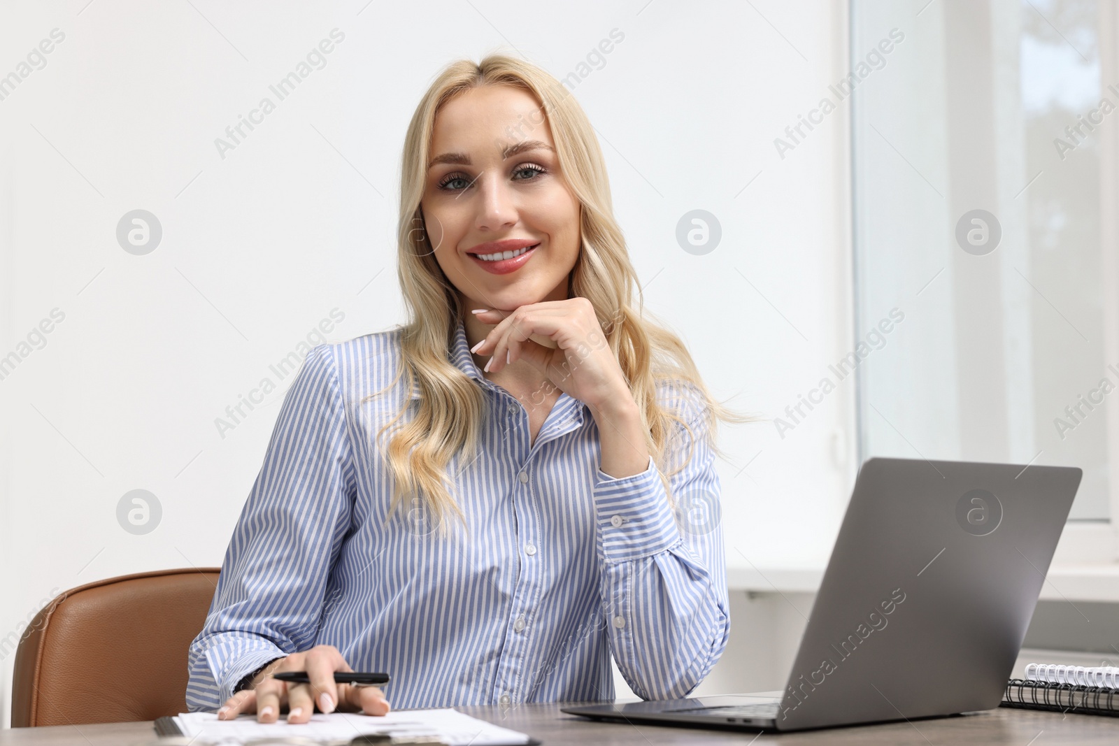 Photo of Happy secretary at table with laptop and stationery in office