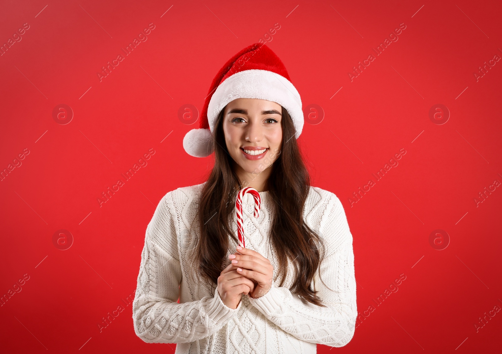 Photo of Beautiful woman in Santa Claus hat holding candy cane on red background