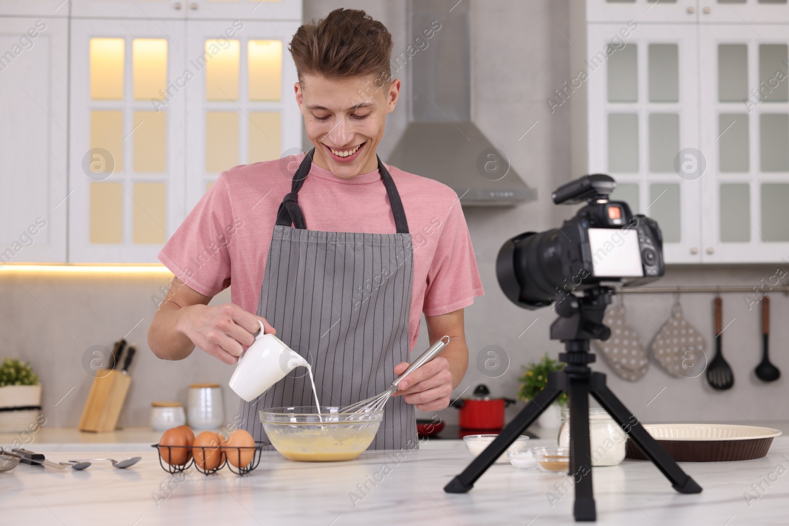 Photo of Smiling food blogger cooking while recording video in kitchen