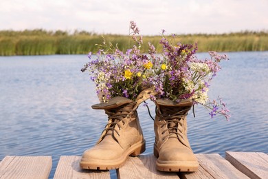 Photo of Boots with beautiful wild flowers on wooden pier near lake