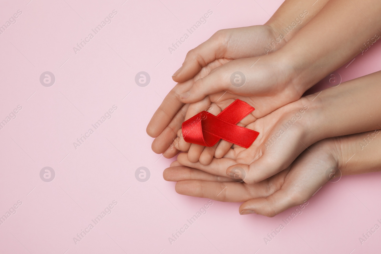 Photo of Woman and girl holding red ribbon on pink background, top view with space for text. AIDS disease awareness