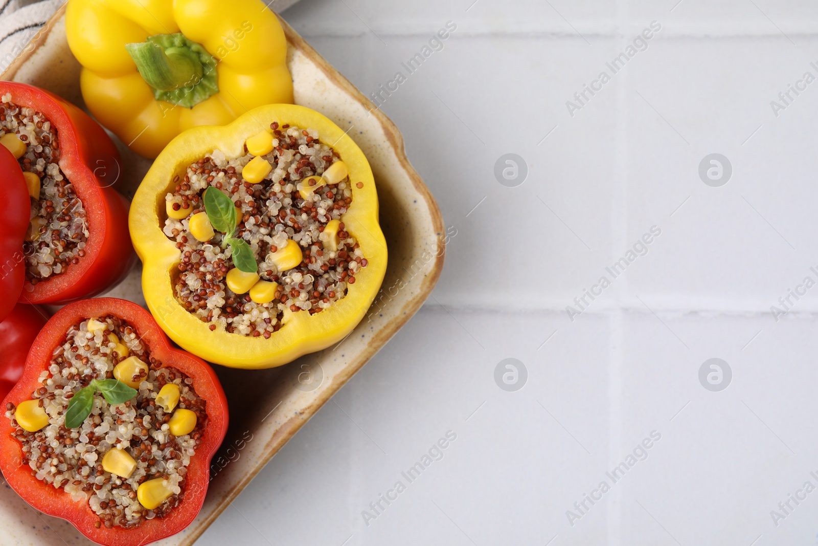 Photo of Quinoa stuffed bell peppers and basil in baking dish on white tiled table, top view. Space for text