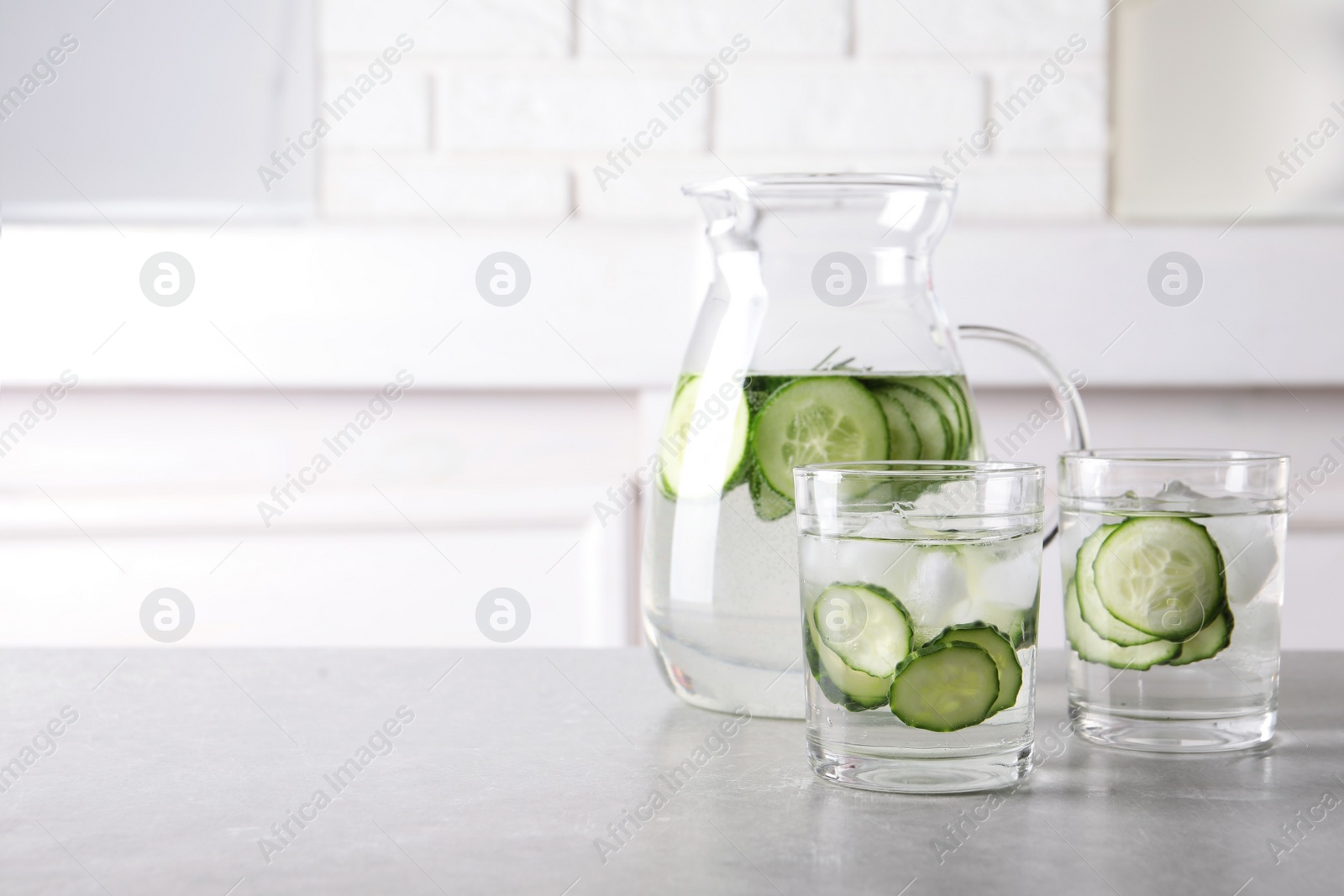 Photo of Glasses and jug of fresh cucumber water on table. Space for text