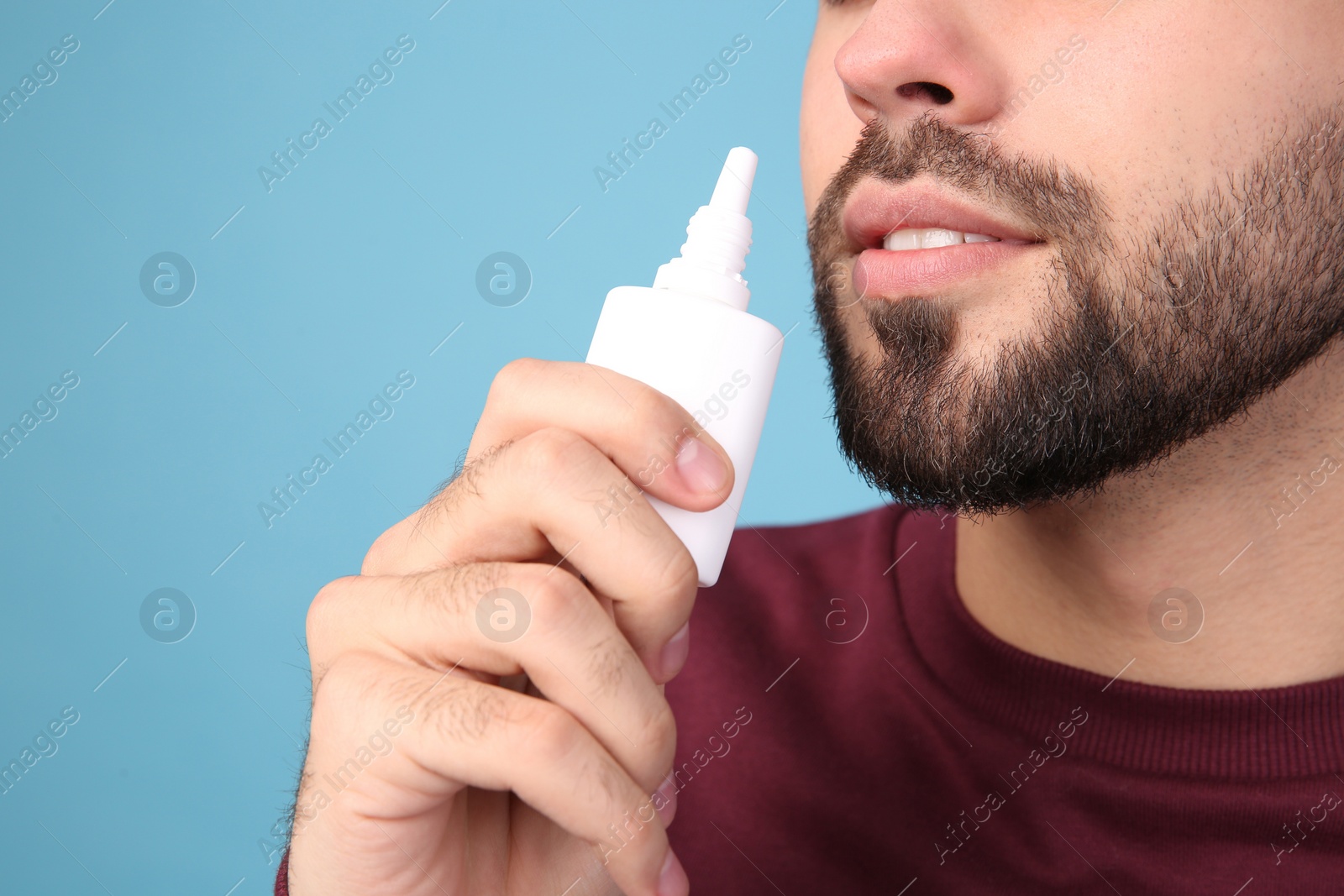 Photo of Man using nasal spray on light blue background, closeup. Space for text