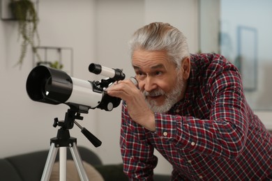 Senior man looking at stars through telescope in room