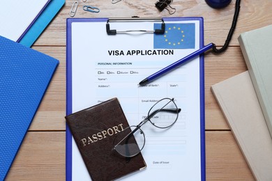 Photo of Visa application form for immigration to European Union, passport, glasses and stationery on wooden table, flat lay