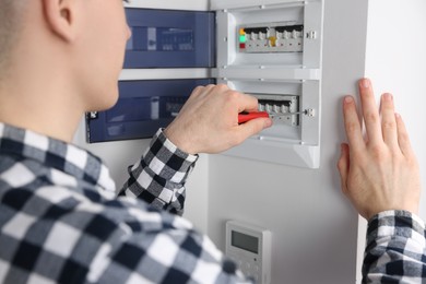 Photo of Young handyman with screwdriver repairing electrical panel board indoors, closeup