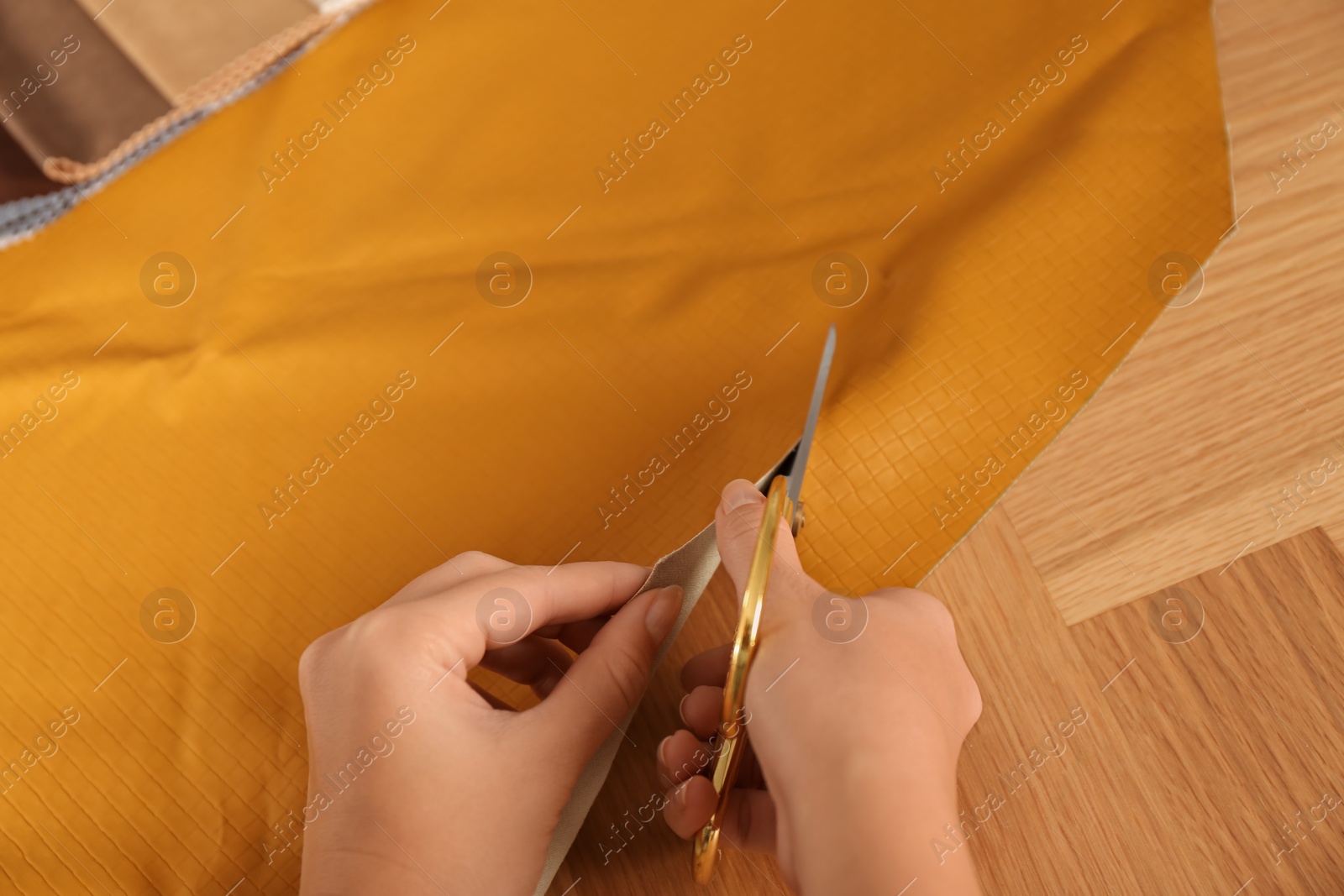 Photo of Woman cutting orange leather with scissors at wooden table, closeup