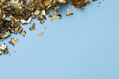 Photo of Many pieces of edible gold leaf on light blue background, top view. Space for text