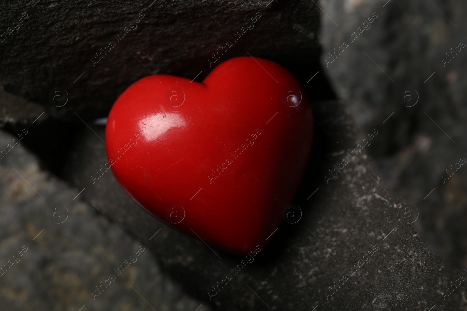 Photo of One red decorative heart between stones, closeup