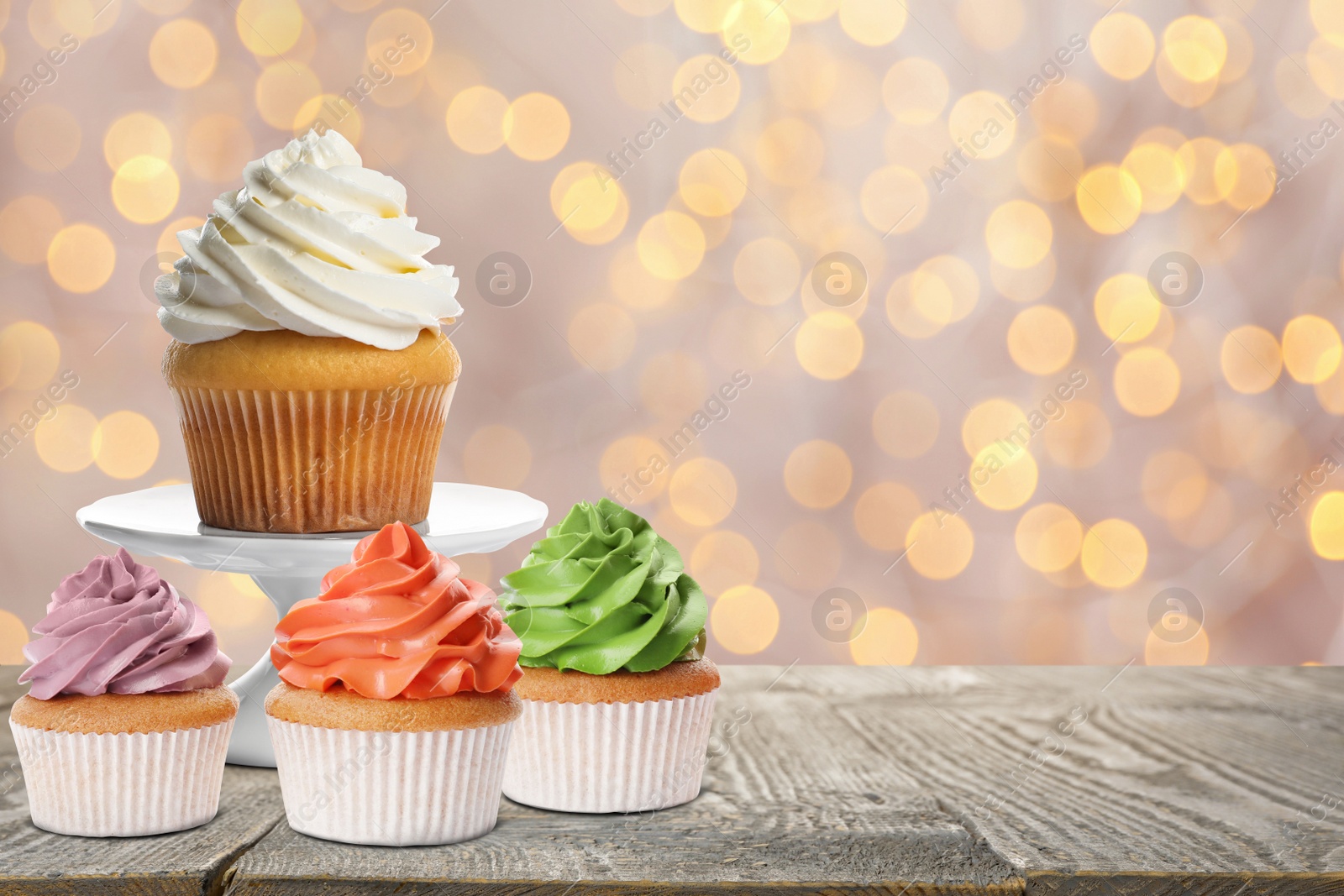 Image of Delicious birthday cupcakes on wooden table against blurred lights. Space for text