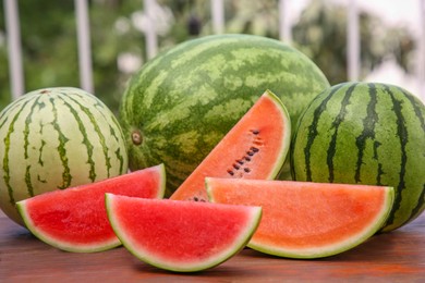 Different cut and whole ripe watermelons on wooden table outdoors