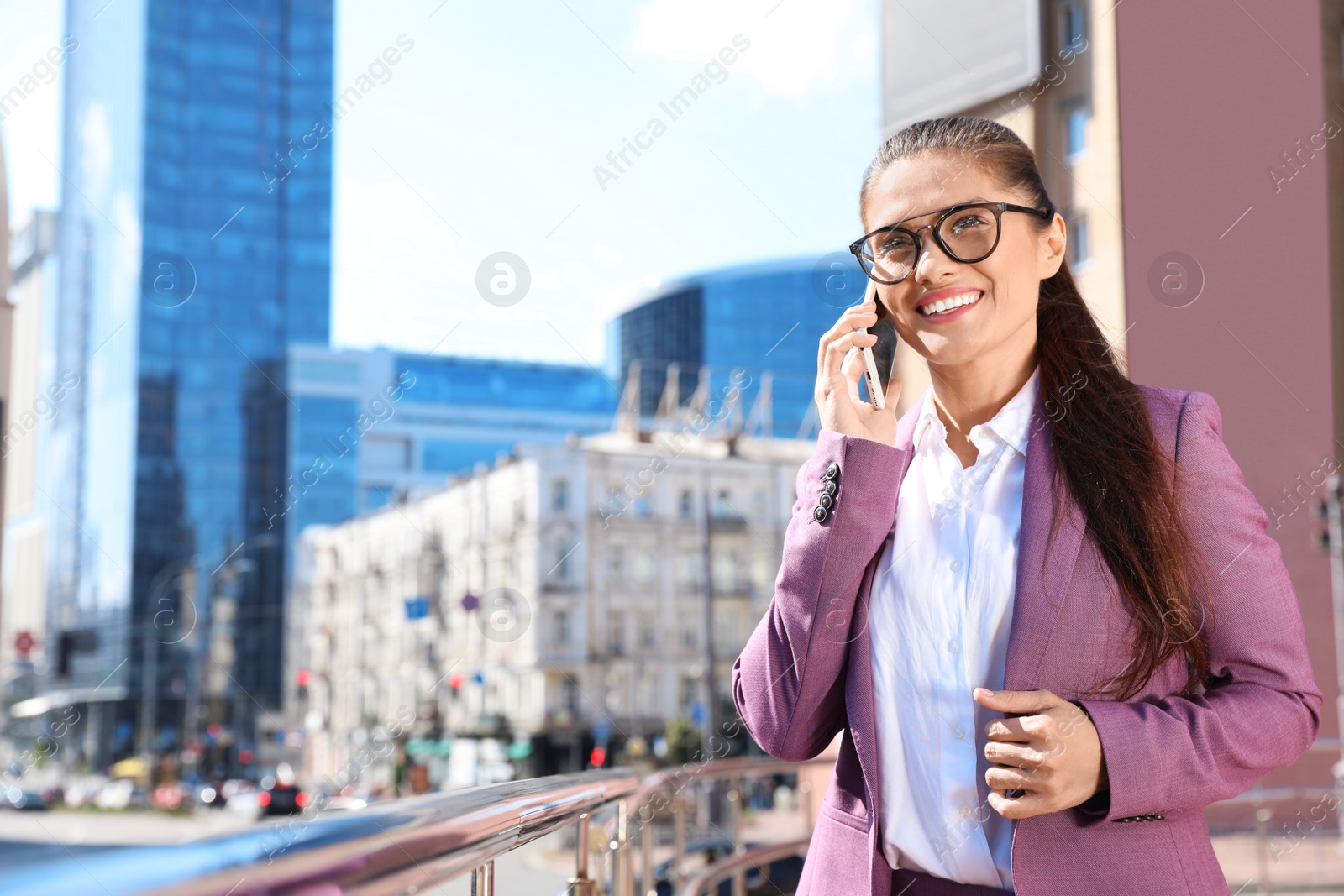 Photo of Beautiful businesswoman talking on phone in city on sunny day