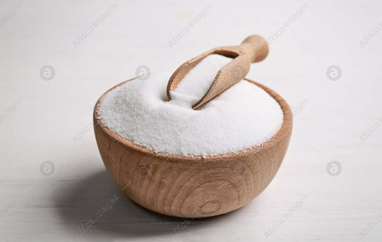Photo of Wooden bowl with natural salt and scoop on white table, closeup