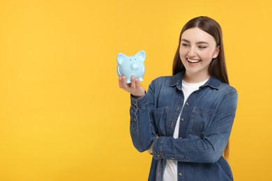 Photo of Happy woman with piggy bank on orange background, space for text