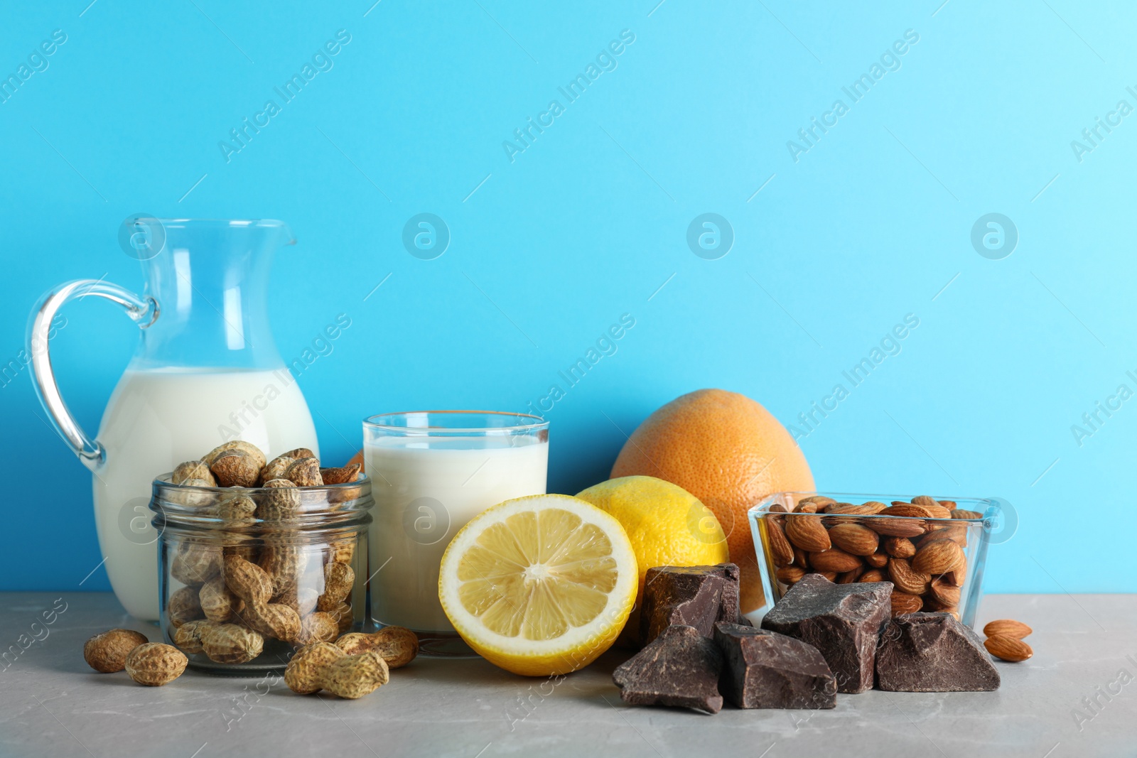 Photo of Different products on stone table against light blue background, space for text. Food allergy concept