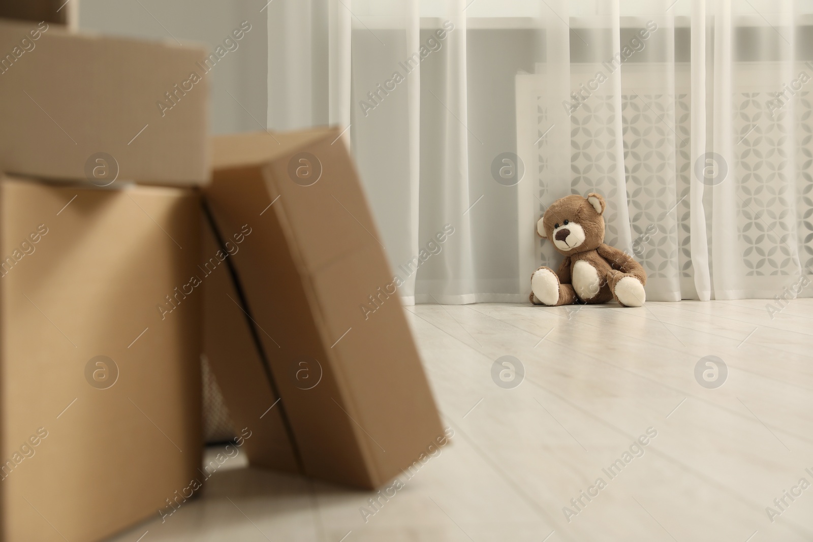 Photo of Cute lonely teddy bear on floor near boxes indoors