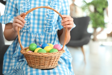 Photo of Beautiful woman holding basket with Easter eggs at home, closeup. Space for text