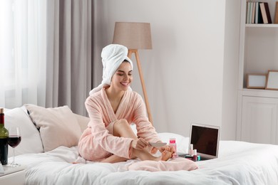 Photo of Beautiful young woman giving herself pedicure on bed at home