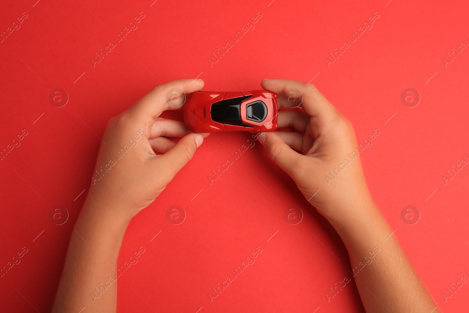 Photo of Child holding toy car on red background, top view