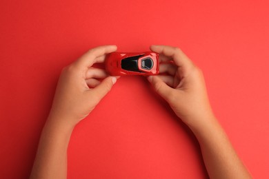 Photo of Child holding toy car on red background, top view